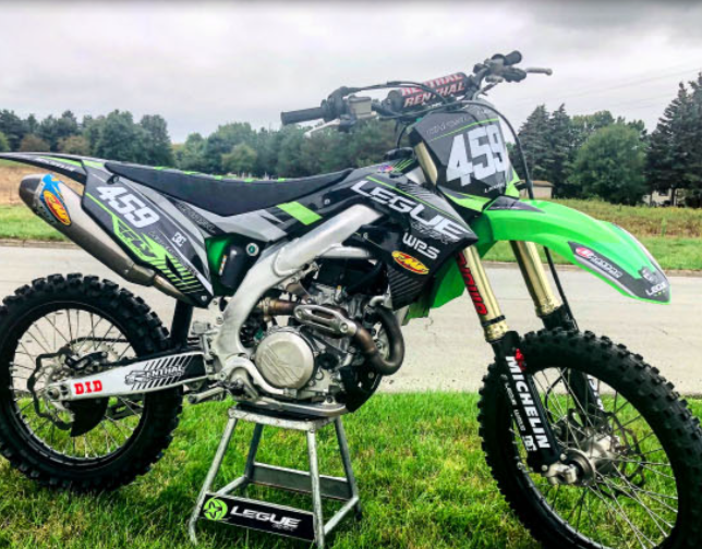 Green and black motocross bike on a stand with 'League Graphics' branding.